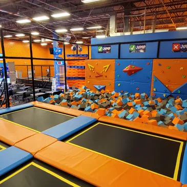 Trampoline area with foam pit and climbing wall at GAME LAB, featuring vibrant orange and blue colors, designed for children's birthday parties and play activities.
