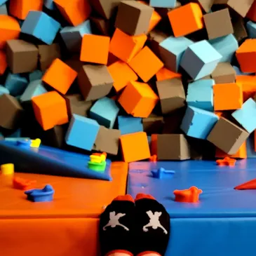 Colorful foam blocks in orange, blue, and gray piled up in a play area, with a pair of grip socks in the foreground, highlighting the fun and safe environment for children's activities at GAME LAB.